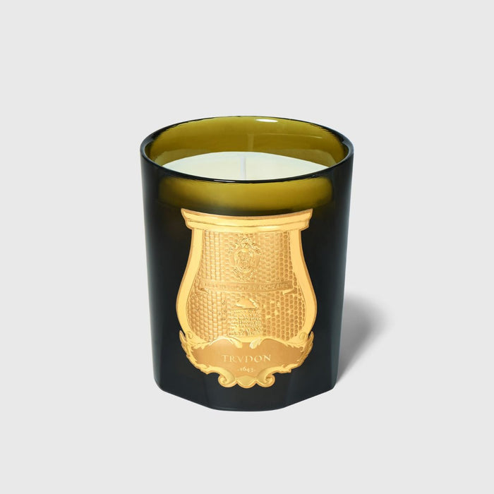 Candle with gold lid and decorative emblem on a light gray background
