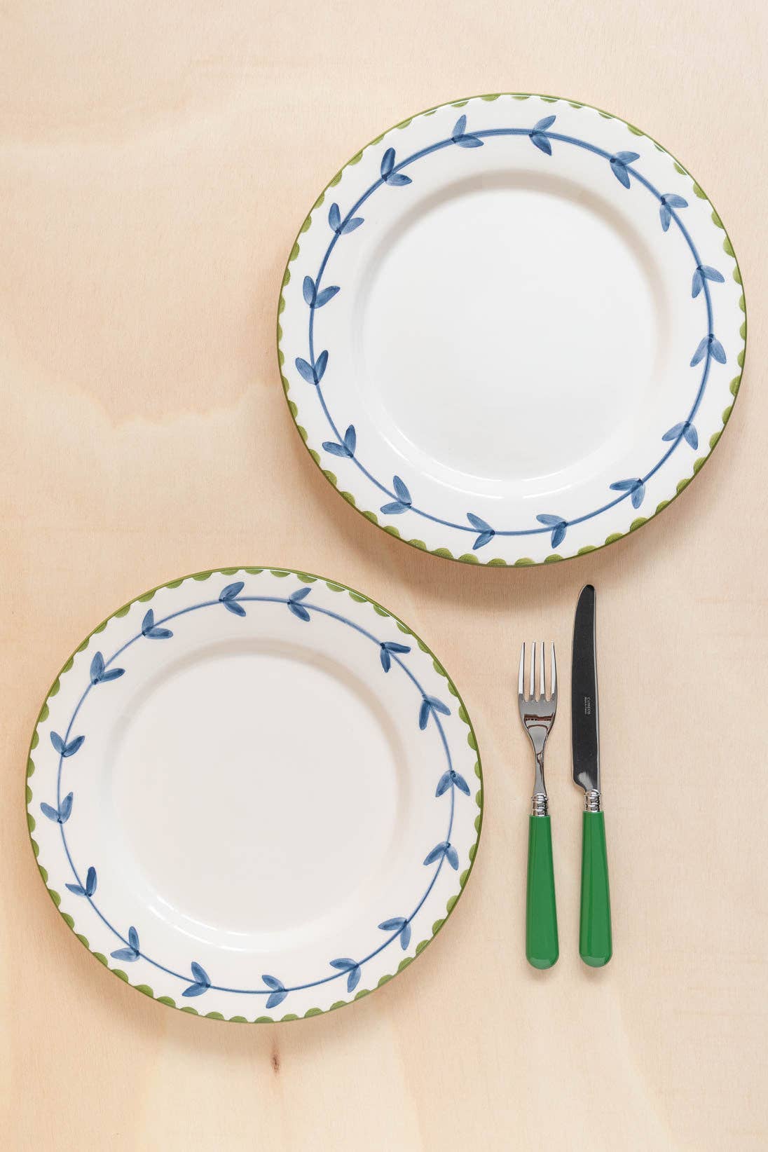 Two white plates with blue and green decorative edges and a fork and knife with green handles on a beige background.