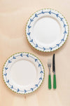 Two white plates with blue and green decorative edges and a fork and knife with green handles on a beige background.