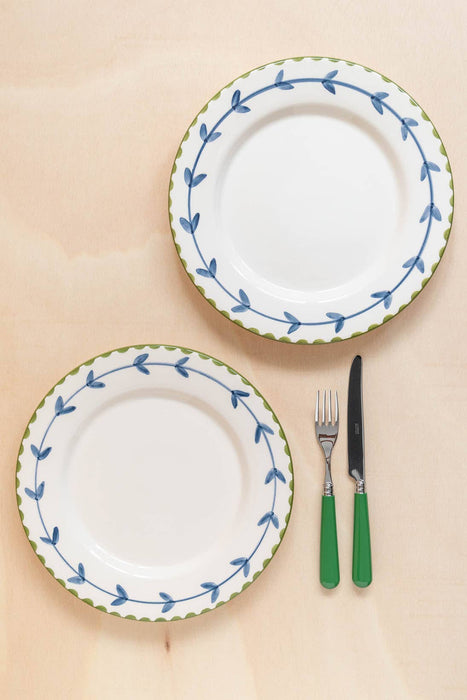 Two white plates with blue and green decorative edges and a fork and knife with green handles on a beige background.