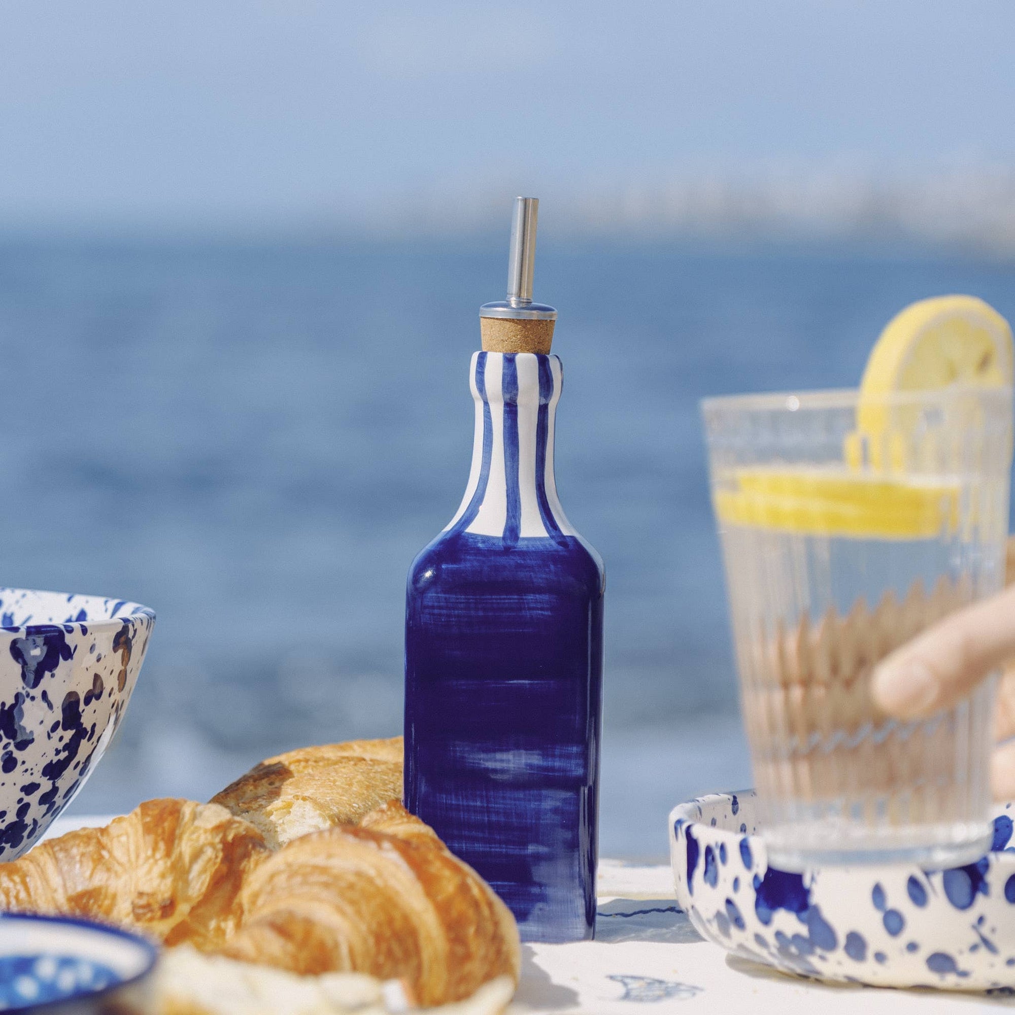 Blue and white striped bottle with a straw on a table by the ocean.