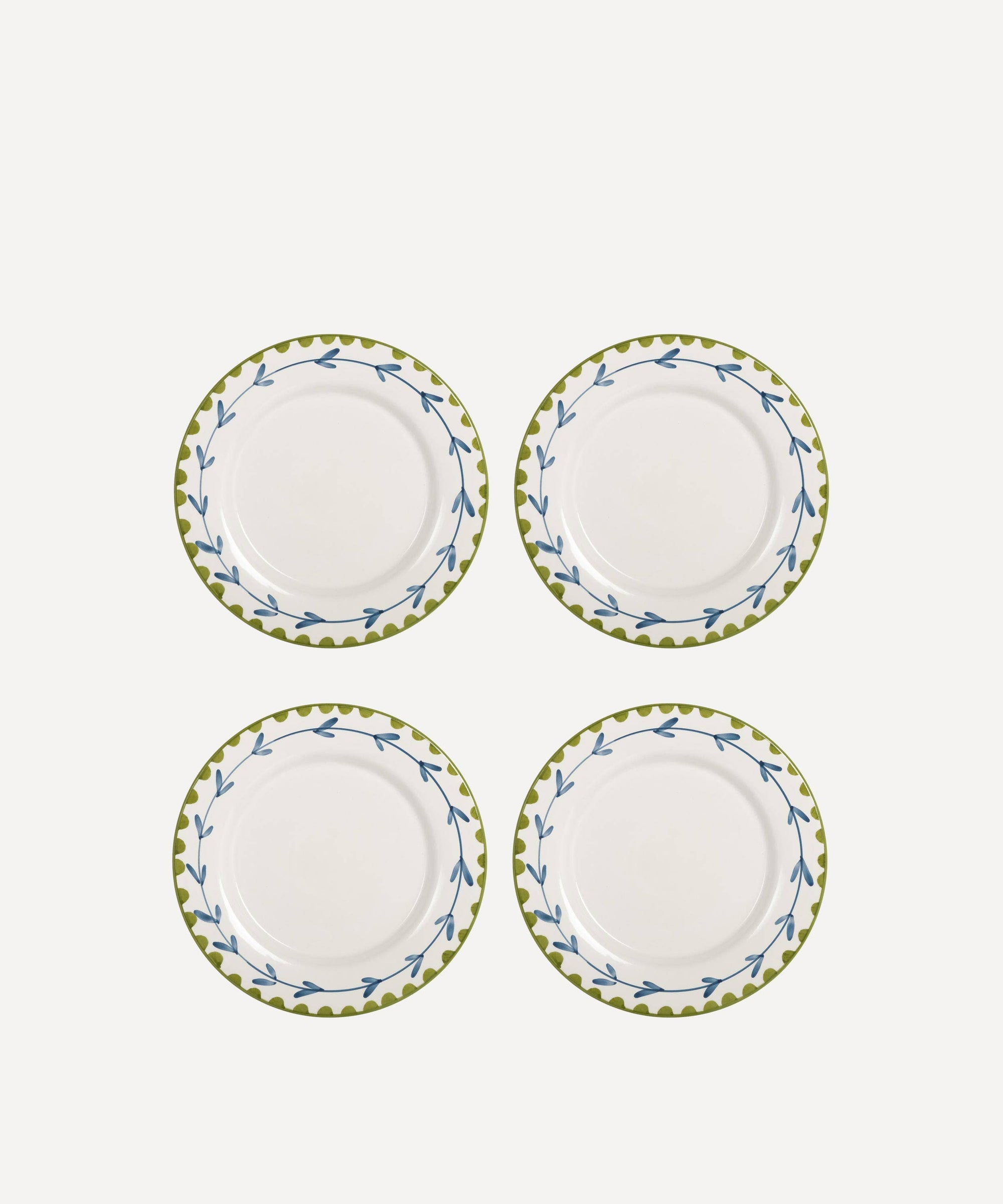 Set of four white plates with green floral rims on a white background