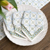 Stack of patterned napkins on a white plate with a floral arrangement in the background.