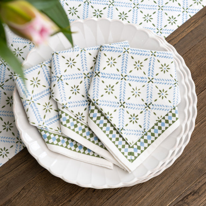 Stack of patterned napkins on a white plate with a floral arrangement in the background.