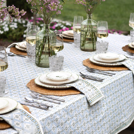 Outdoor dining table setting with floral centerpieces and patterned tablecloth.