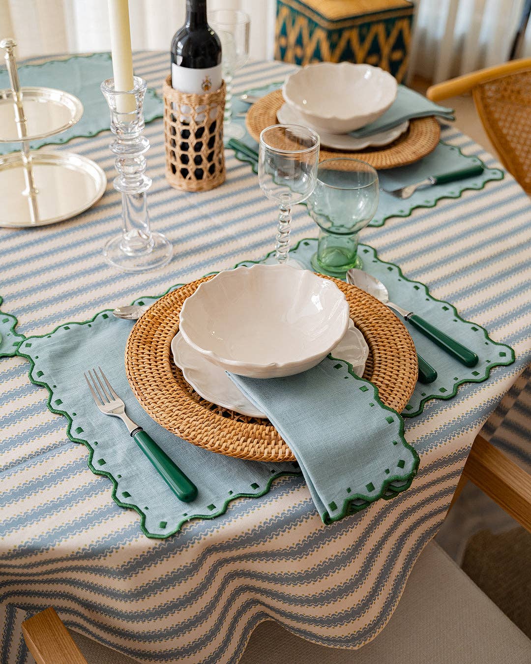 Dining table setting with striped tablecloth, wicker placemats, and ceramic plates.