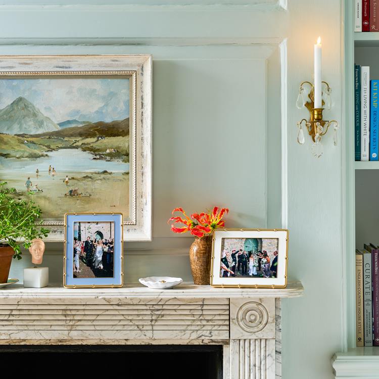 Decorative mantelpiece with framed pictures, a vase with flowers, and a candle.