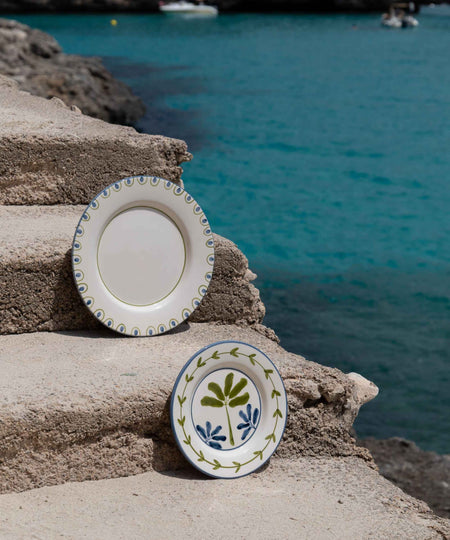 Two ceramic plates with decorative patterns on a stone ledge by the sea.