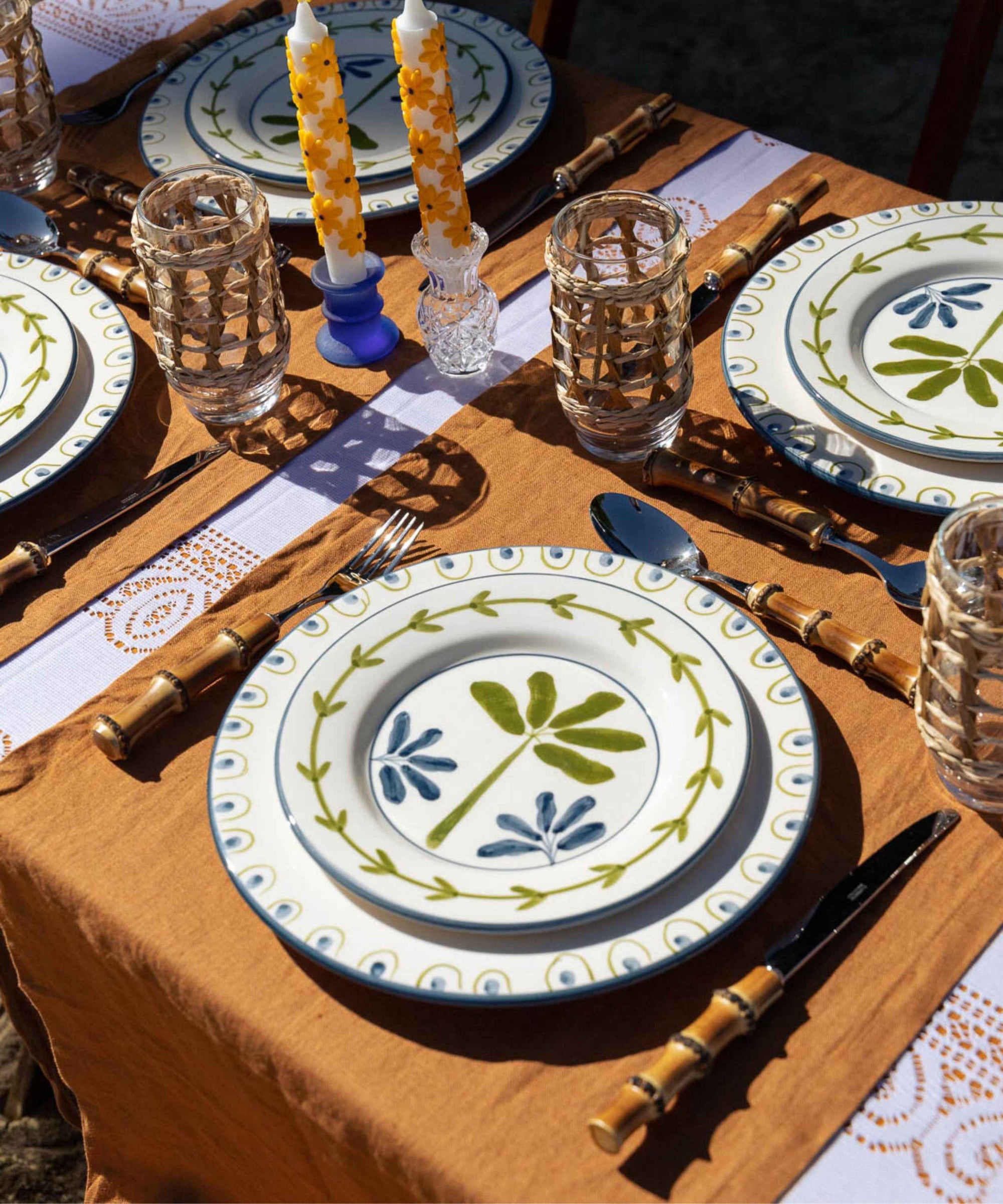 Dining table setting with decorative plates, glasses, and cutlery on a brown tablecloth.
