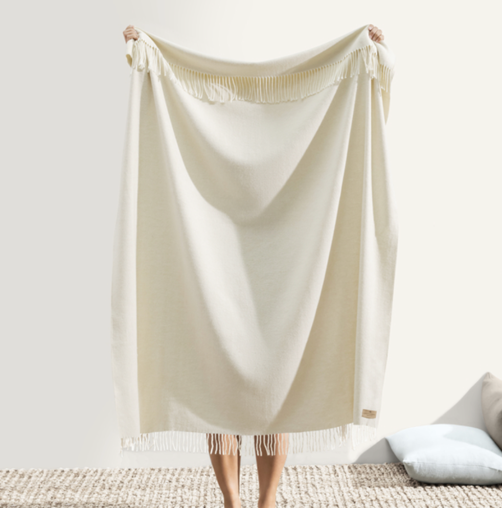 Person holding a beige blanket in a minimalistic room.