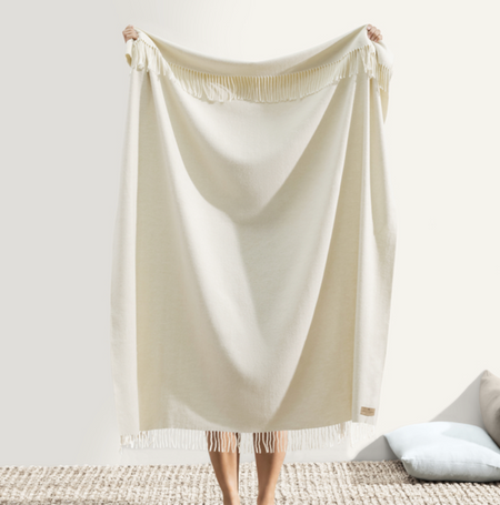 Person holding a beige blanket in a minimalistic room.