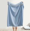 Person holding a light blue throw blanket with fringe on a neutral background