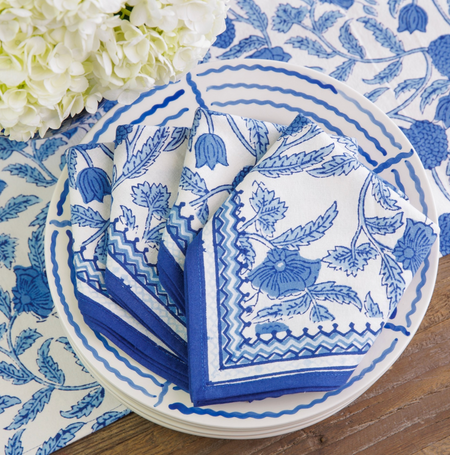 Blue and white patterned napkins on a matching plate with flowers in the background