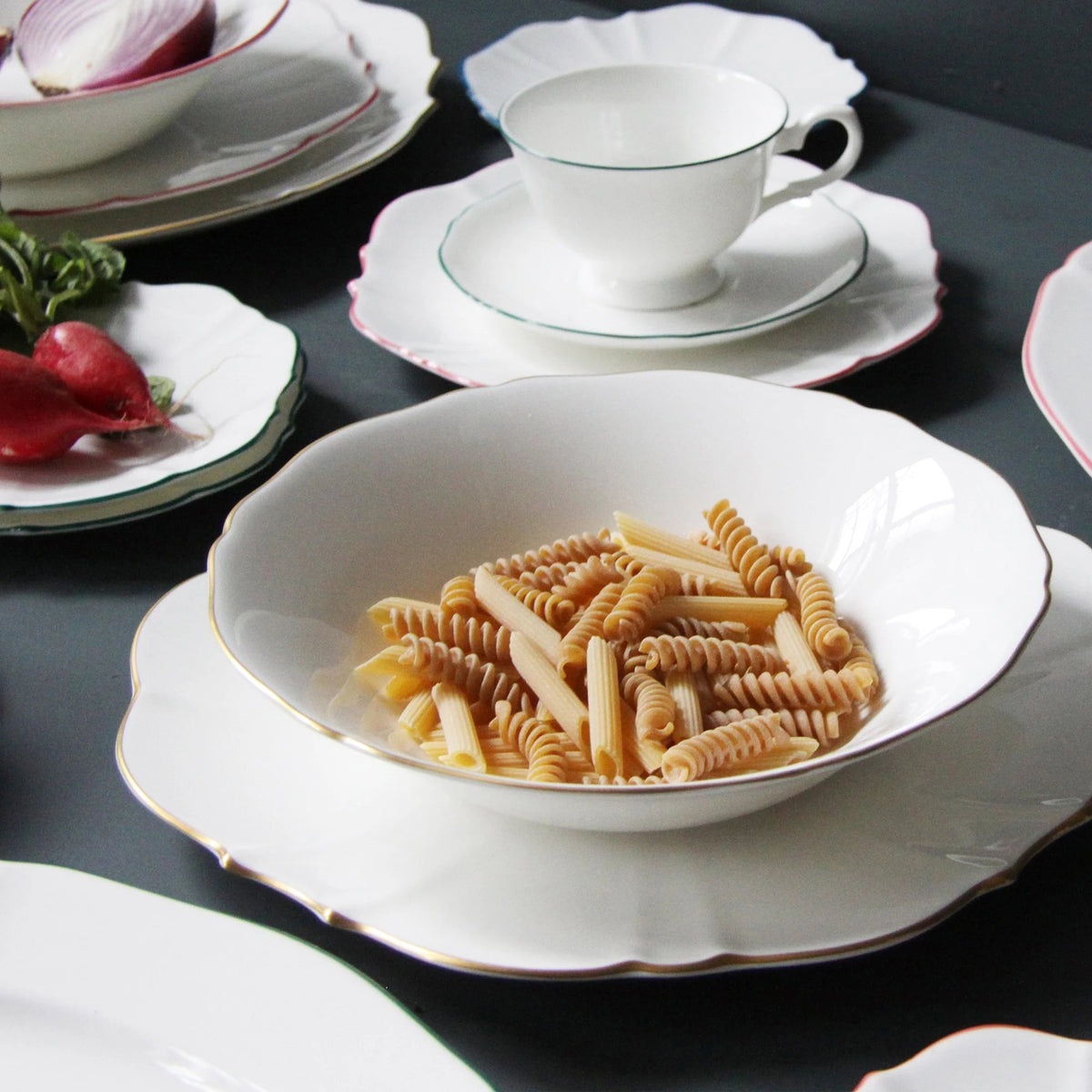 White bowl with gold rim with pasta in it on table with plates