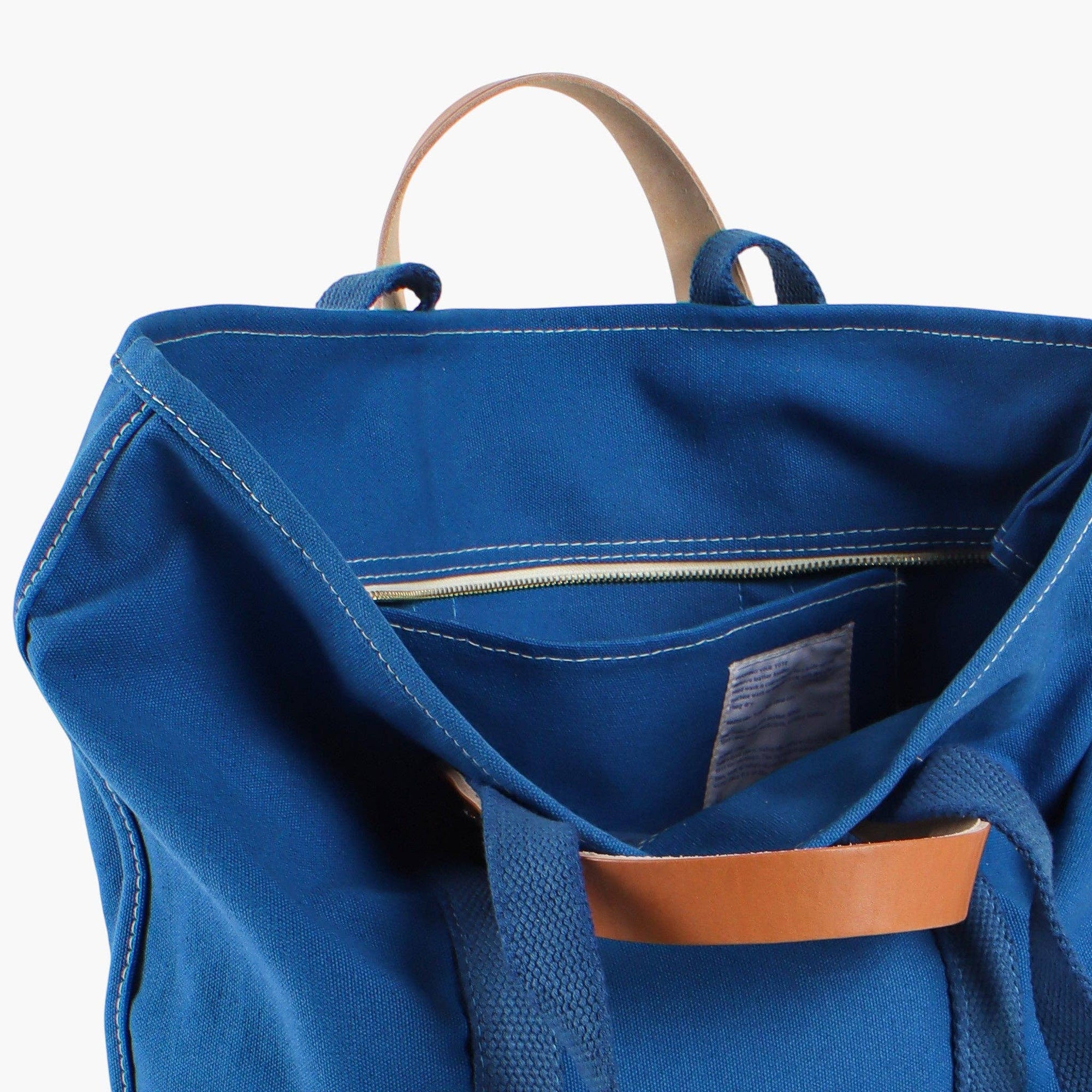 Canvas blue tote bag with leather handles and canvas shoulder strap with inside pocket and zipper on white background 