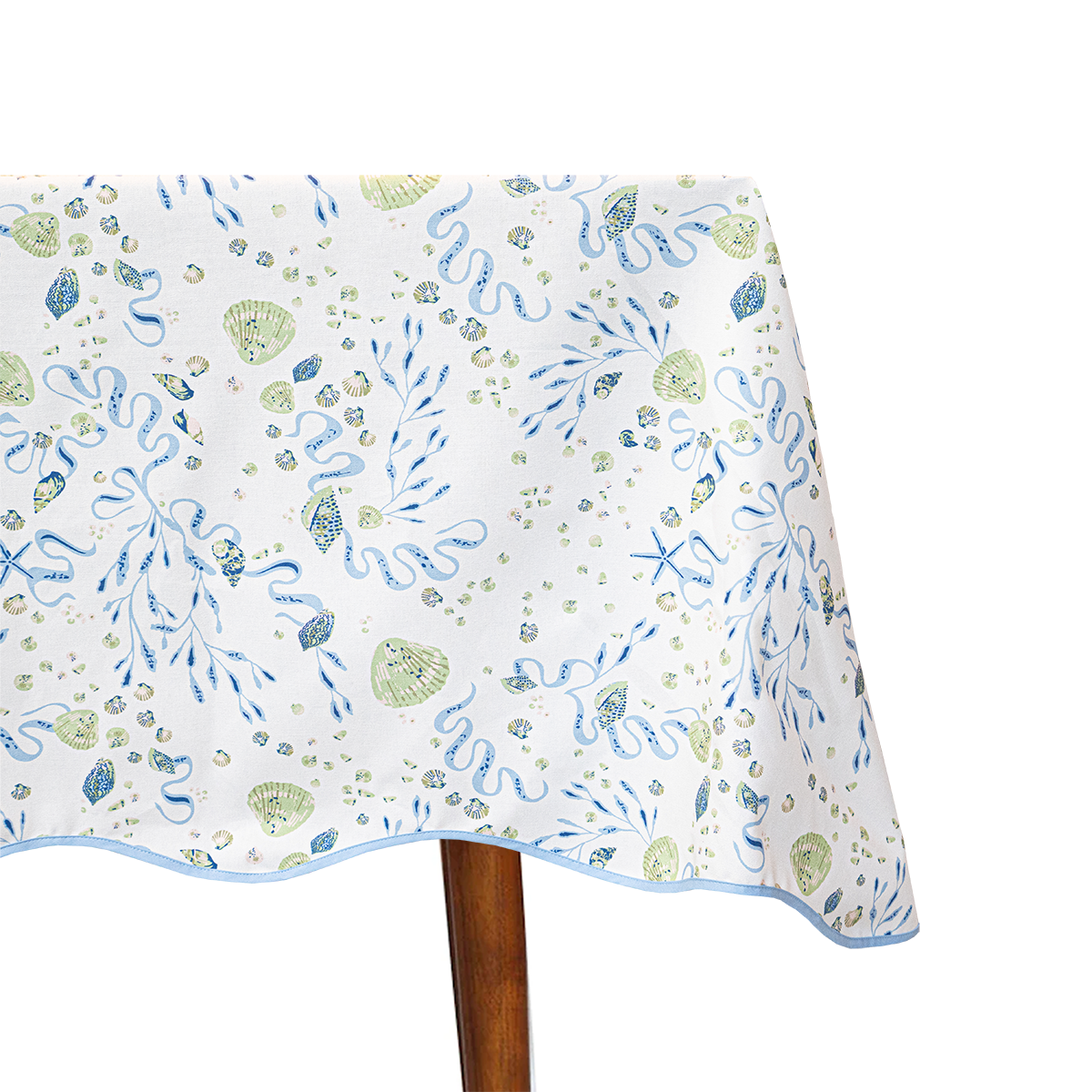 Tablecloth with green and blue shell detail and a scalloped edge on table on white background 
