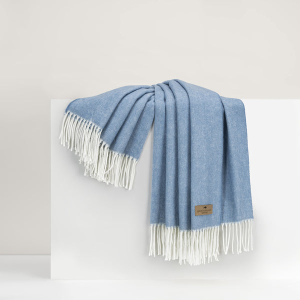 A blue and white striped throw with decorative fringe draped over a white surface.