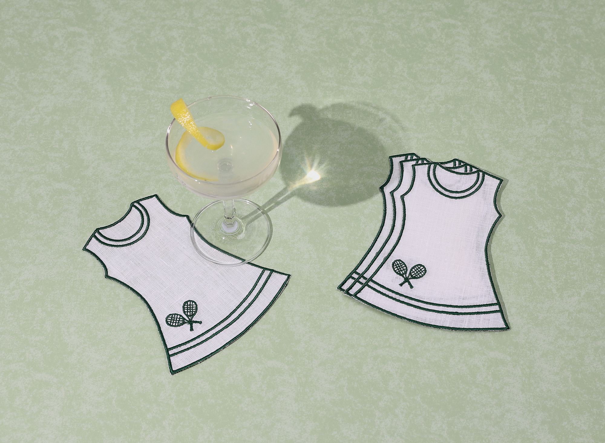 Four tennis dress cocktail napkins on green background with drink with lemon twist. 