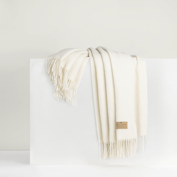 A beige cashmere throw with fringe draped over a white surface.