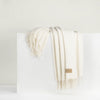 A beige cashmere throw with fringe draped over a white surface.