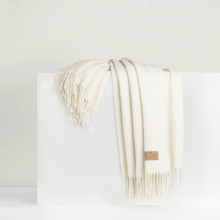 A beige cashmere throw with fringe draped over a white surface.