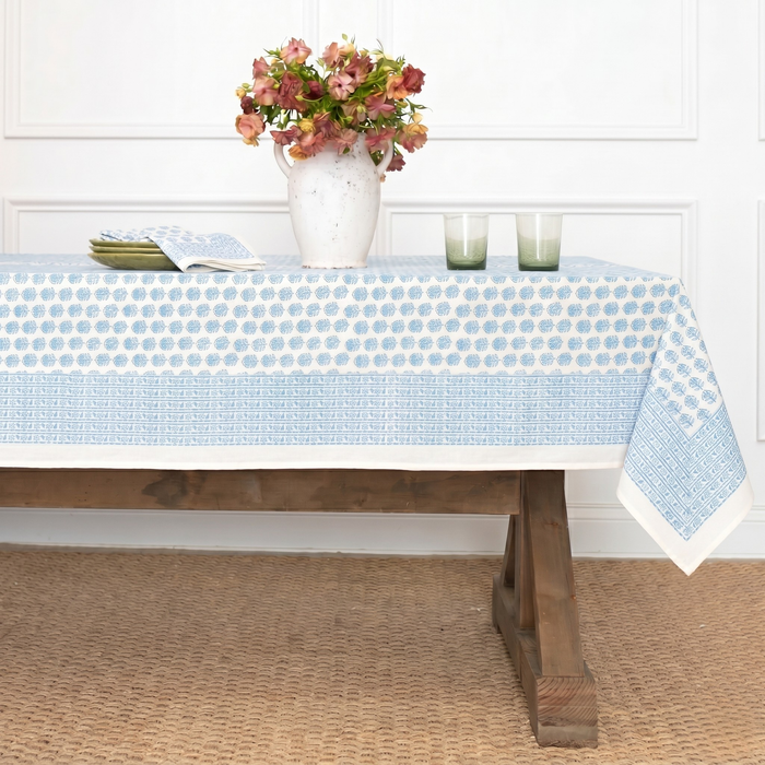 Table with a blue and white polka dot tablecloth, flowers, and candles on a wooden floor.