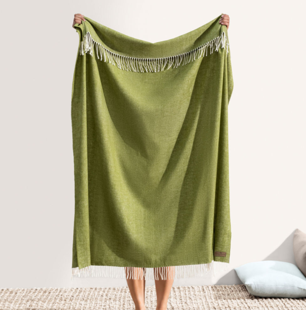 Green blanket with fringe held by a person on a neutral background