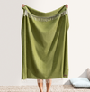 Green blanket with fringe held by a person on a neutral background