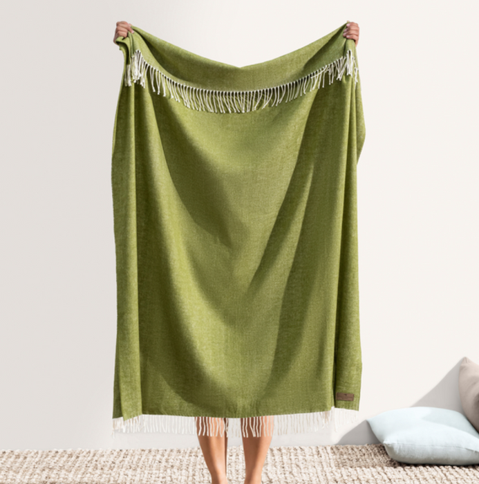 Green blanket with fringe held by a person on a neutral background
