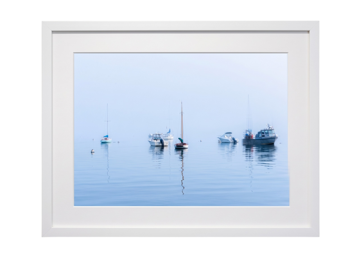 A framed photographic print of calm blue water with several small boats floating on the horizon, presented in a wide white frame against a light gray background.