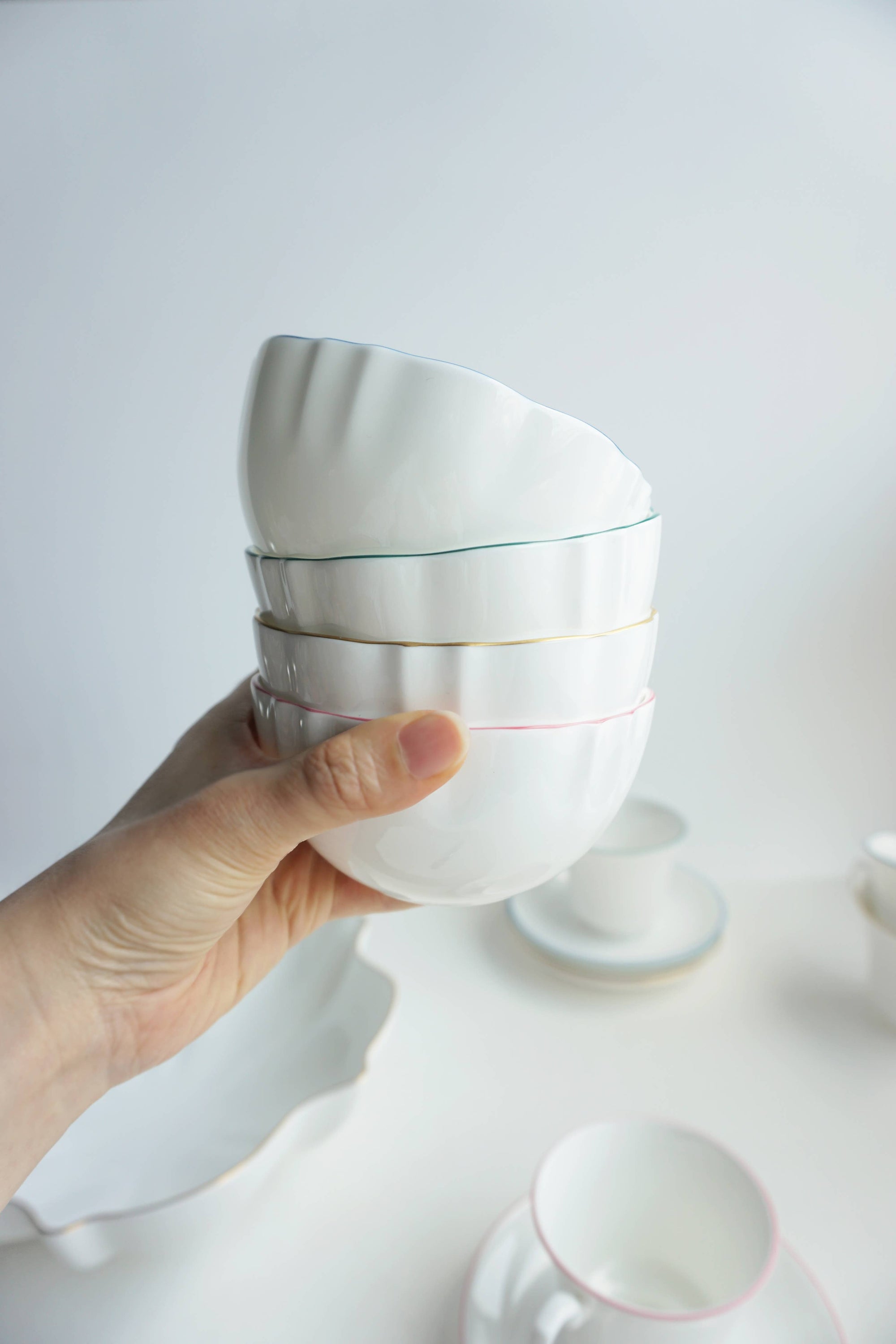 A hand holding a fine bone china bowl with a royal blue rim, with other bowls and a plate in the background.