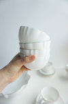 A hand holding a fine bone china bowl with a royal blue rim, with other bowls and a plate in the background.