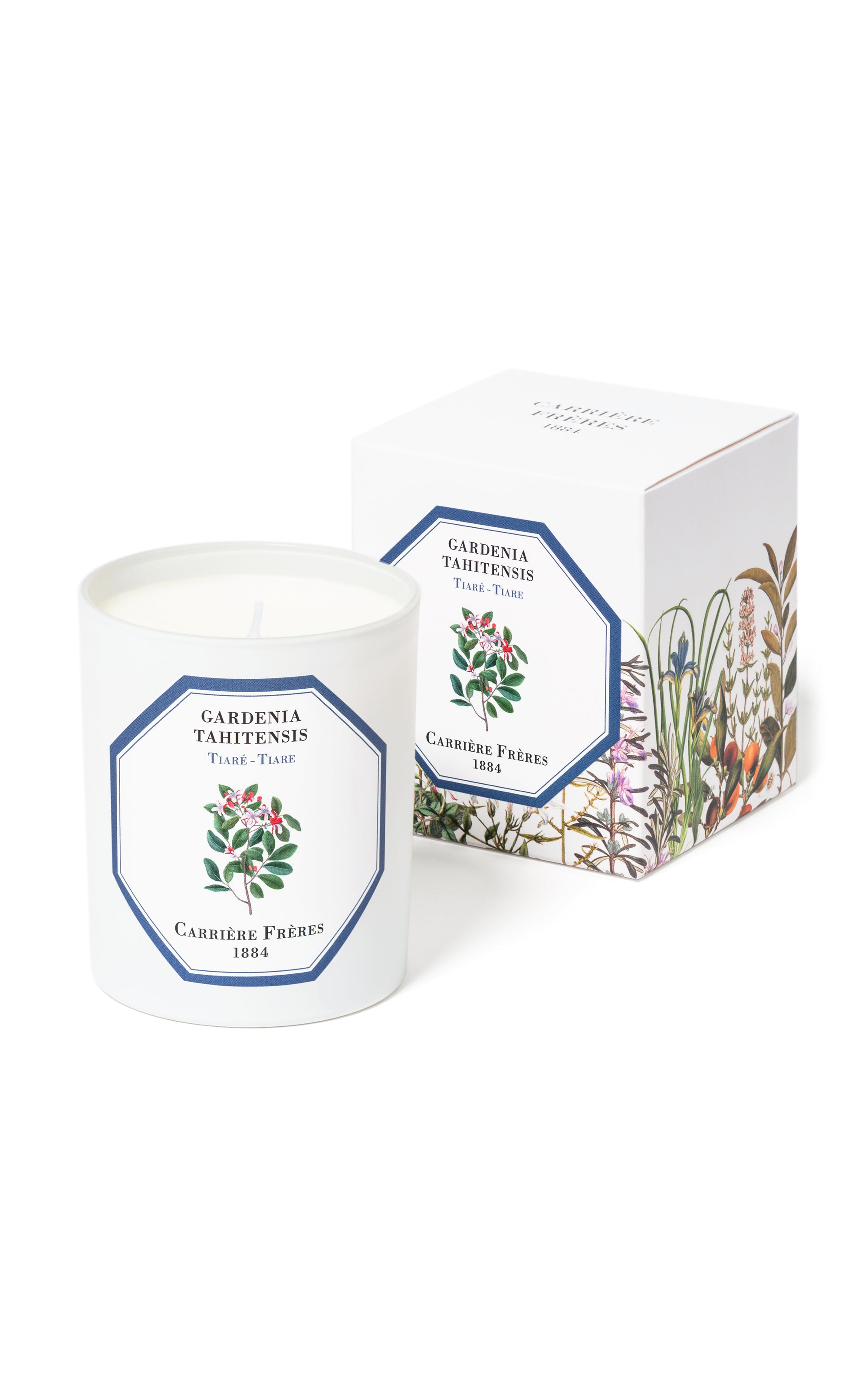 A white candle with a blue label, depicting a tiare flower, presented in front of its floral-themed packaging.