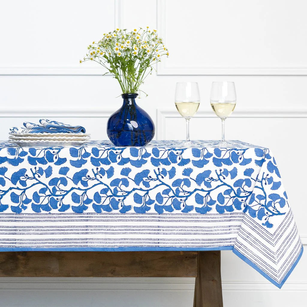 Table setting with a blue and white floral tablecloth, vase, and glasses.