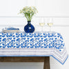 Table setting with a blue and white floral tablecloth, vase, and glasses.