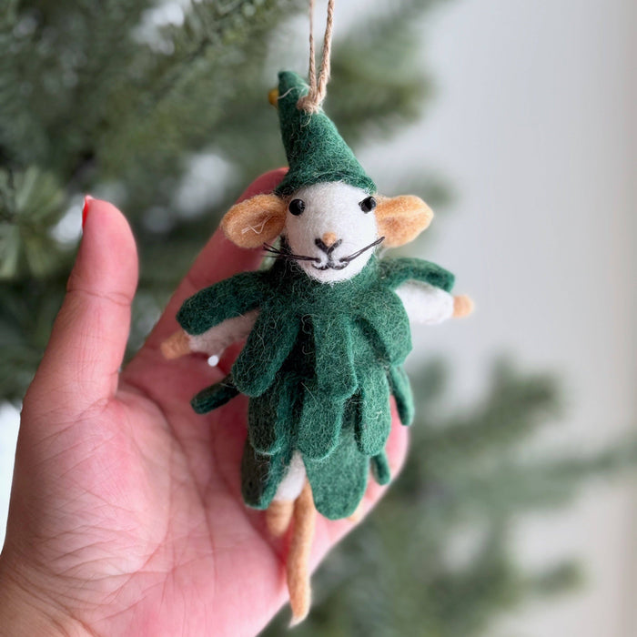 Felt mouse ornament in a green outfit held against a blurred Christmas tree background