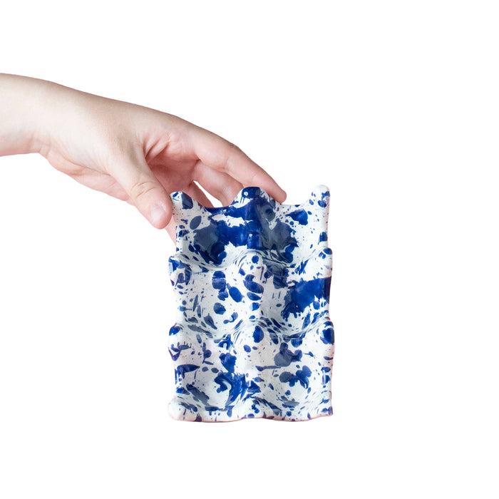Hand holding a blue and white ceramic pouch against a white background