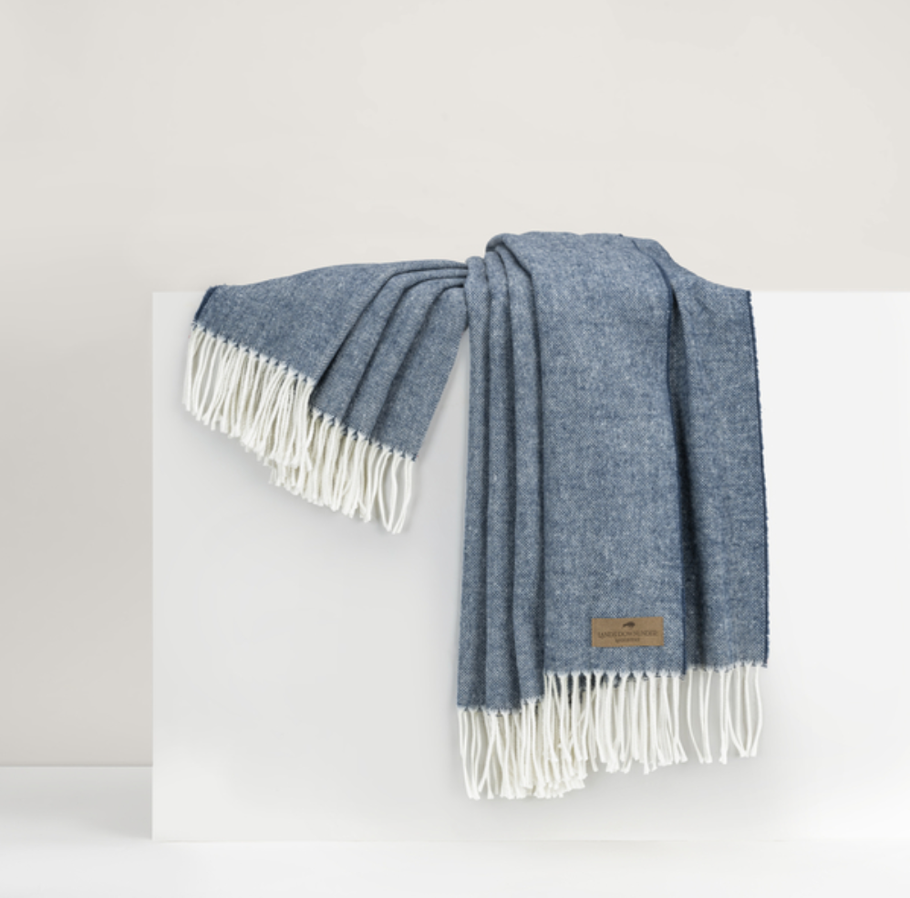 A blue and white herringbone pattern throw with fringe draped over a white surface.