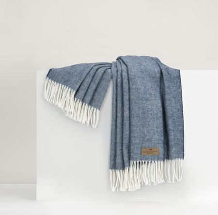 A blue and white herringbone pattern throw with fringe draped over a white surface.