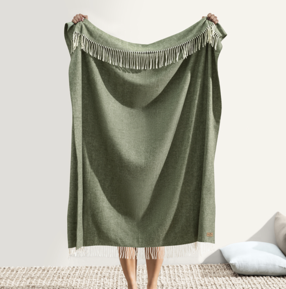 Green blanket with fringe held by a person on a neutral background