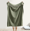 Green blanket with fringe held by a person on a neutral background
