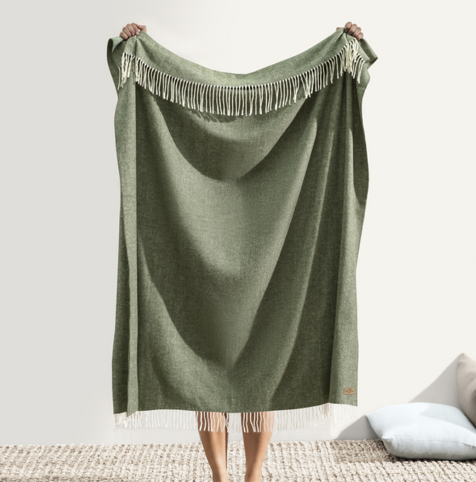 Green blanket with fringe held by a person on a neutral background
