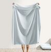 Person holding a light blue satin sheet over a bed with a neutral background