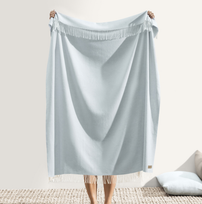 Person holding a light blue satin sheet over a bed with a neutral background
