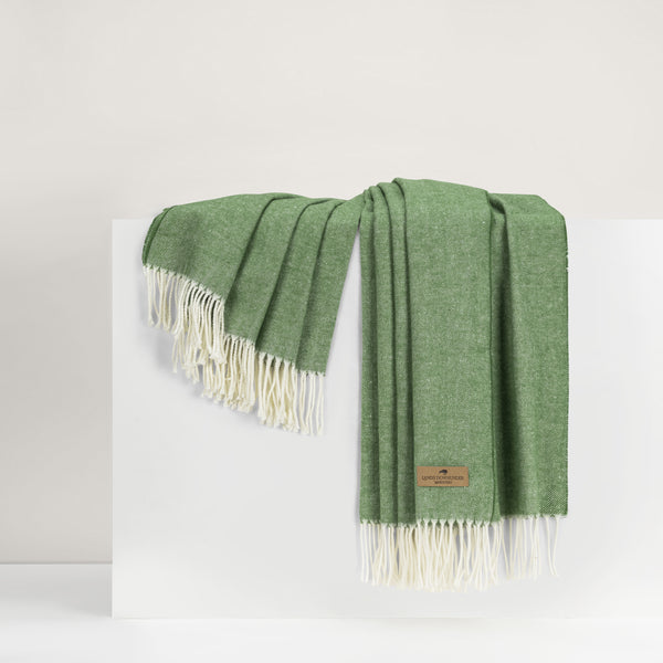 Green throw blanket with white fringes on a light gray background