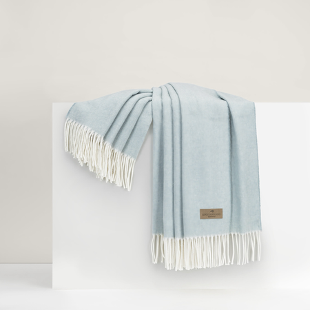 Light blue throw blanket with white fringe on a white surface