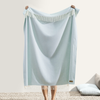 Person holding a light blue towel with white fringe on a neutral background