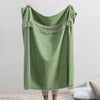 Green blanket with fringe held by a person against a plain background