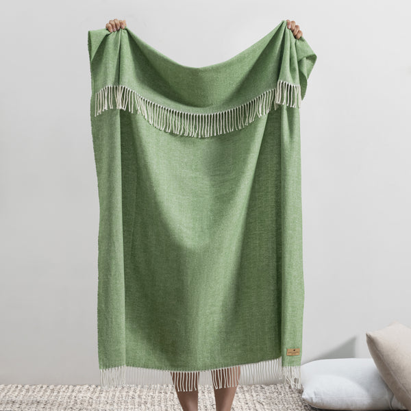 Green blanket with fringe held by a person against a plain background