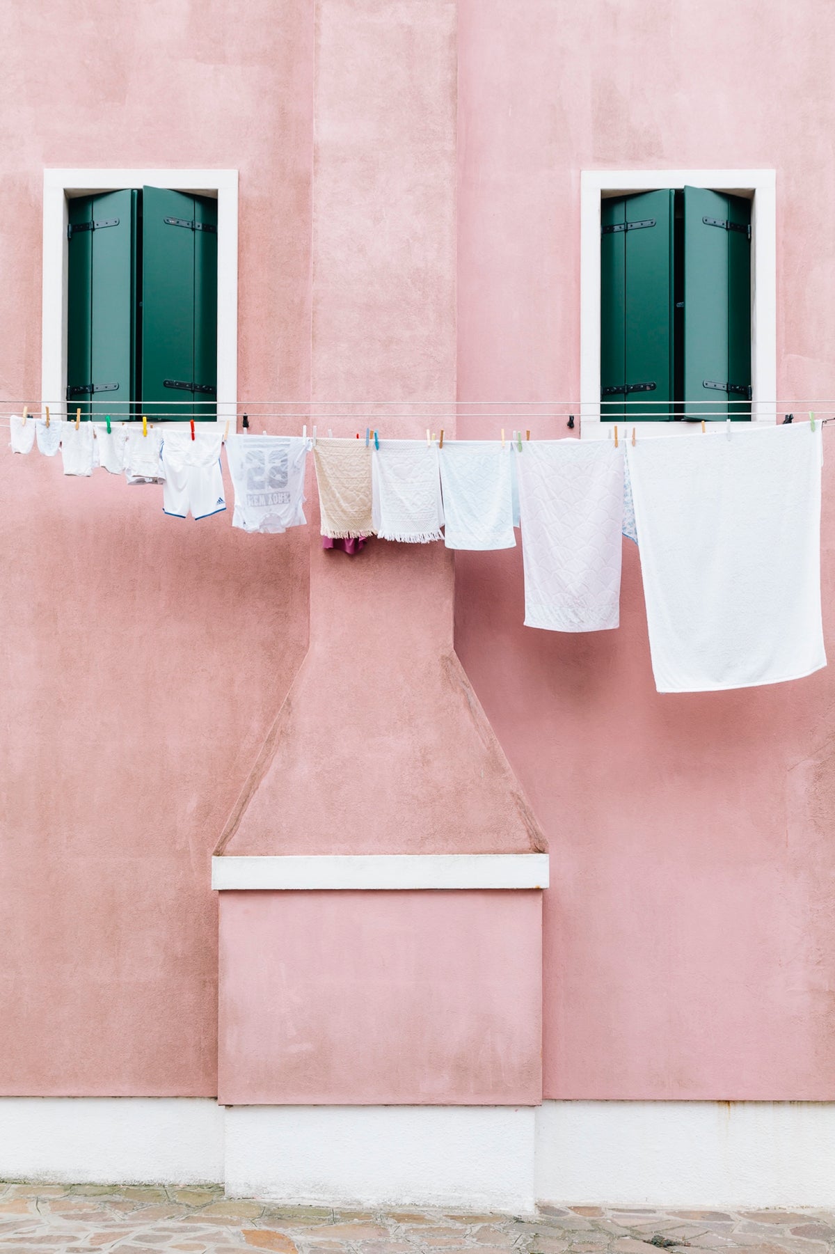 White laundry hanging on a clothesline against a pink wall with two windows.